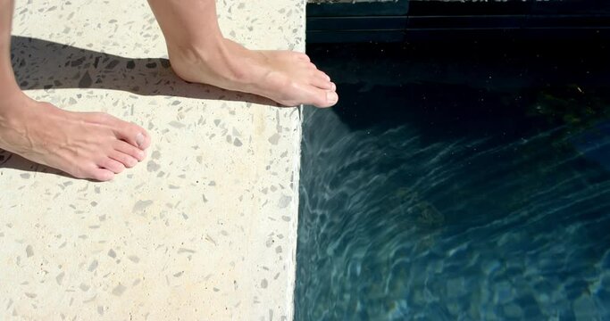 Bare feet are poised on the edge of a swimming pool, ready to dip into the water