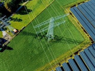 Aerial view of solar panels beside an electricity pylon on lush green fields
