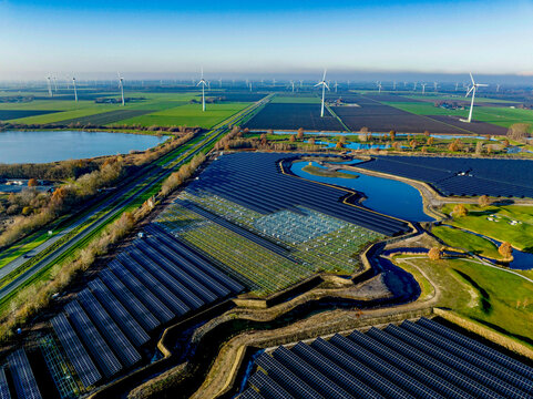 Aerial view of a sprawling solar farm alongside wind turbines in a green landscape.