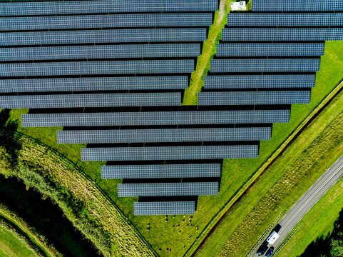 Aerial view of a solar farm flanking a road with cars in motion
