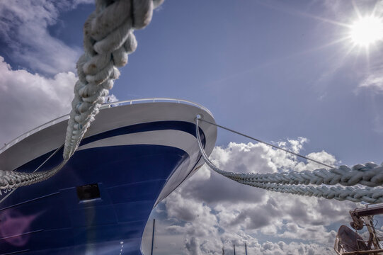 A ship moored under a sunny sky, viewed through the sturdy ropes that secure it