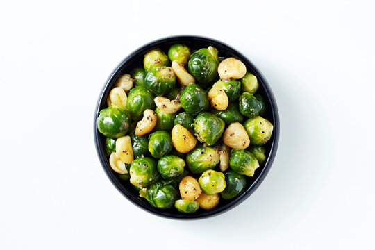 A bowl of roasted brussels sprouts and garlic cloves on a white background