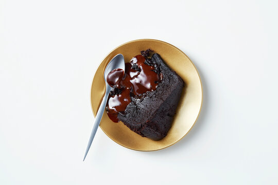 A slice of delectable chocolate cake oozing with rich sauce on a golden plate.