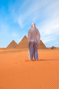 A muslim woman walks up a hill on the sand in the Sahara desert - Giza Pyramid Complex at amazing sunset - Cairo, Egypt