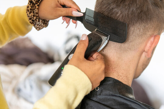 A person is receiving a haircut from a hairstylist using electric clippers and a comb.