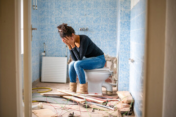 Exhausted homeowner sits on a toilet in an unfinished bathroom