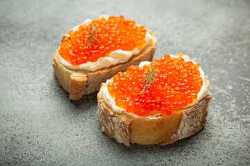 Two caviar toasts baguette canape with butter and red salmon caviar top view on grey concrete background, festive luxury delicacy and appetizer. - 757233670