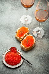 Small metal plate with red salmon caviar, two caviar toasts canape, two glasses of champagne top view on grey concrete background, festive luxury delicacy and appetizer. - 757234051