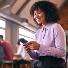 Smiling Businesswoman With Mobile Phone Working In Open Plan Office With Colleagues In Background - 757234437