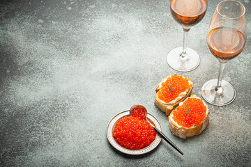 Small metal plate with red salmon caviar, two caviar toasts canape, two glasses of champagne top view on grey concrete background, festive luxury delicacy and appetizer. Space for text. - 757234618