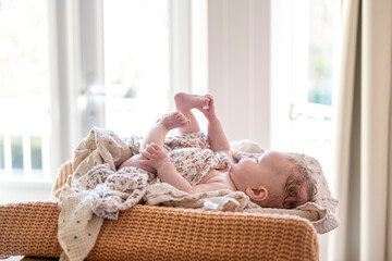 Baby lying playfully on a wicker daybed by the window.