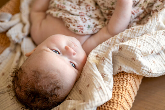 Baby relaxed on a cozy blanket gazing upwards with interest.