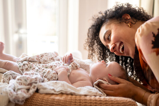 A joyful moment as a mother interacts with her baby lying in a cozy home setting.