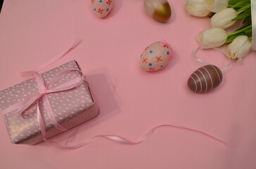 Easter, Easter egg color is bright, spring Orthodox holiday. colorful decorated eggs on a pink background. Happy Easter, white tulips. gift box tied with ribbon