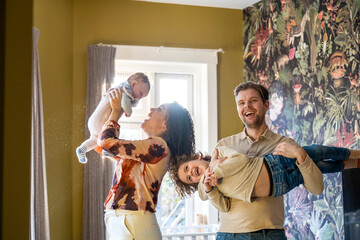 Family fun time as a parent lifts a joyful child into the air in a cozy home setting.