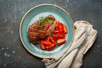 Delicious roasted duck breast fillet with golden crispy skin, with pepper and rosemary, top view on ceramic blue plate served with cherry tomatoes salad, rustic concrete rustic background - 757236801
