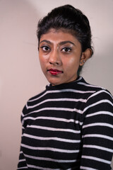 A woman with black and white stripes on her shirt is standing in front of a white wall. She has red lipstick on and her eyes are closed