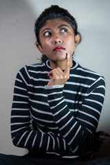 A woman with a black and white striped shirt is sitting on the floor and looking up. She is thinking about something