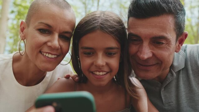 Close up, happy family using smart phone looking at pictures and videos sitting in park bench