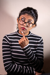 A woman with glasses is looking at the camera and pointing her finger. She is wearing a striped shirt and has red nail polish on her nails. Concept of curiosity and playfulness