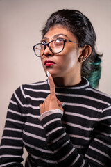A woman with glasses and a red lipstick is looking at the camera. She is wearing a striped shirt and has her hand on her chin. Concept of contemplation and introspection