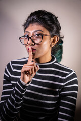 A woman in a striped shirt is holding her hand to her mouth and making a "shush" sound