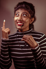 A woman with glasses and a black and white striped shirt is smiling and pointing her finger. She is wearing a red lipstick and has a black and white striped shirt