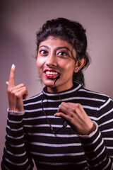 A woman with a black and white striped shirt is pointing her finger and smiling. She is wearing a red lipstick and a necklace