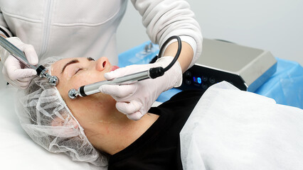 Beautiful woman receiving facial microcurrent treatment at spa salon. Beautician using electrical...