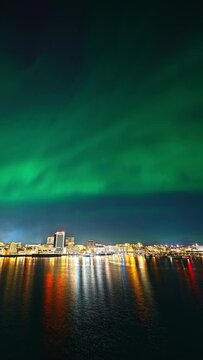 A green pulsating aurora over central Bod&oslash;, with citylights reflecting in the fjord beneath the city in March.
