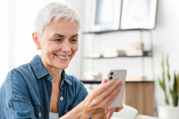 Fototapeta na wymiar Closeup shot of mature Caucasian female housewife using cellphone for ordering delivery online from home. Middle-aged woman doing remote shopping on webpages