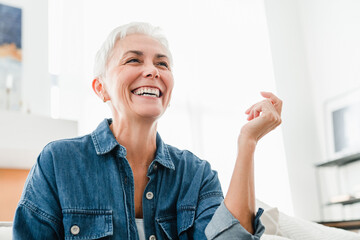 Smiley Caucasian mature woman laughing sitting on the couch. Happy middle-aged woman having...