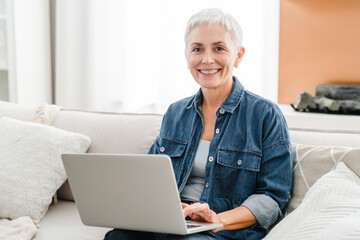 Cheerful mature woman housewife using laptop for online shopping. Middle-aged freelancer working...