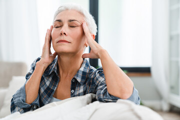 Tired Caucasian woman rubbing temples having headache at home. Exhausted depressed mature...