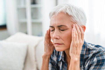 Mature woman rubbing temples from headache at home. Middle-aged housewife suffering from migraine...