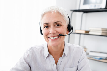 Cropped shot of Caucasian mature businesswoman in headset looking at camera in office. E-learning,...