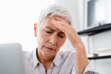 Closeup portrait of Caucasian mature businesswoman having severe headache at workplace. Middle-aged...