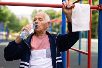 Old man drinking water beside pullup bar outdoors
