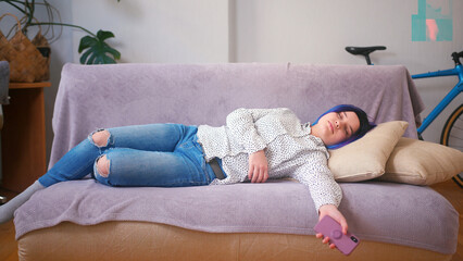 Sleepy latin hispanic teenager girl exhausted or bored rests on sofa with phone in one hand. Cozy...
