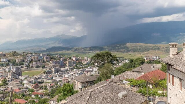 Panorama showing Gjirokastra city from the viewpoint with many typical historic houses with stone roofs of Gjirokaster timelapse. Albania aerial view to valley with rain clouds and shower motion