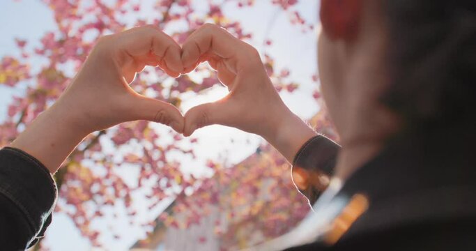 Springtime in the City - Cherry Blossom - A handheld OTS of a woman holding her hands in the shape of a heart. Hands in focus - Slow-mo - Filmed in public space / on public ground