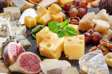 Variety of sliced cheeses with fruits, mint, nuts and cheese cutting knives.