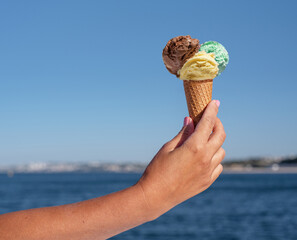 Ice cream cone with colorful ice cream balls in the hand at blue sky background.
