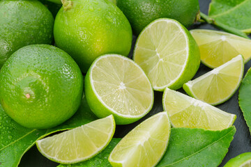Ripe lime fruits with slices and lime leaves on a gray stone table.