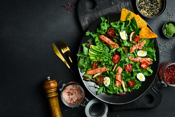 Fresh healthy salad. Salad with arugula, salted salmon, avocado, quail eggs and mushrooms. In a black plate. Diet food.