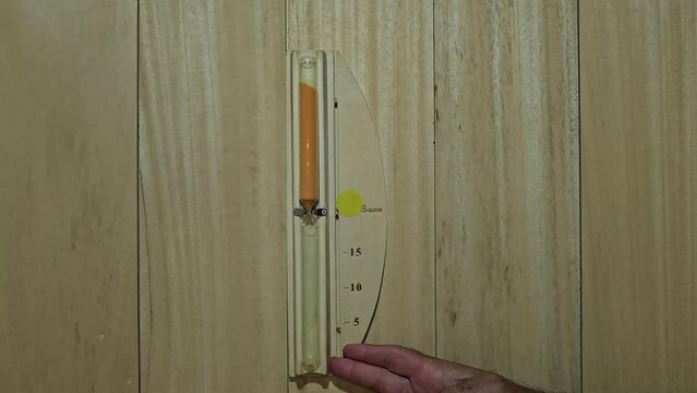Bath thermometer, hourglass decorated on interior wooden wall of private sauna room.