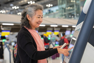 asian senior woman doing self check in at self service check in machine or KIOSK at the airport,elderly retired people with modern lifestyle,technology,transportation,travel