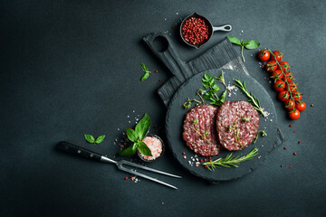 Raw burger patty with spices and herbs on a slate plate. On a dark stone background. Top view.