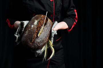 Fragrant black oval bread in female hands. Homemade rye bread.