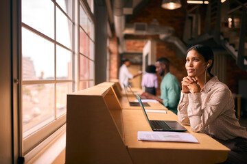 Businesswoman Working In Modern Multi-Cultural Office Listening To Music On Earphones Or Earbuds